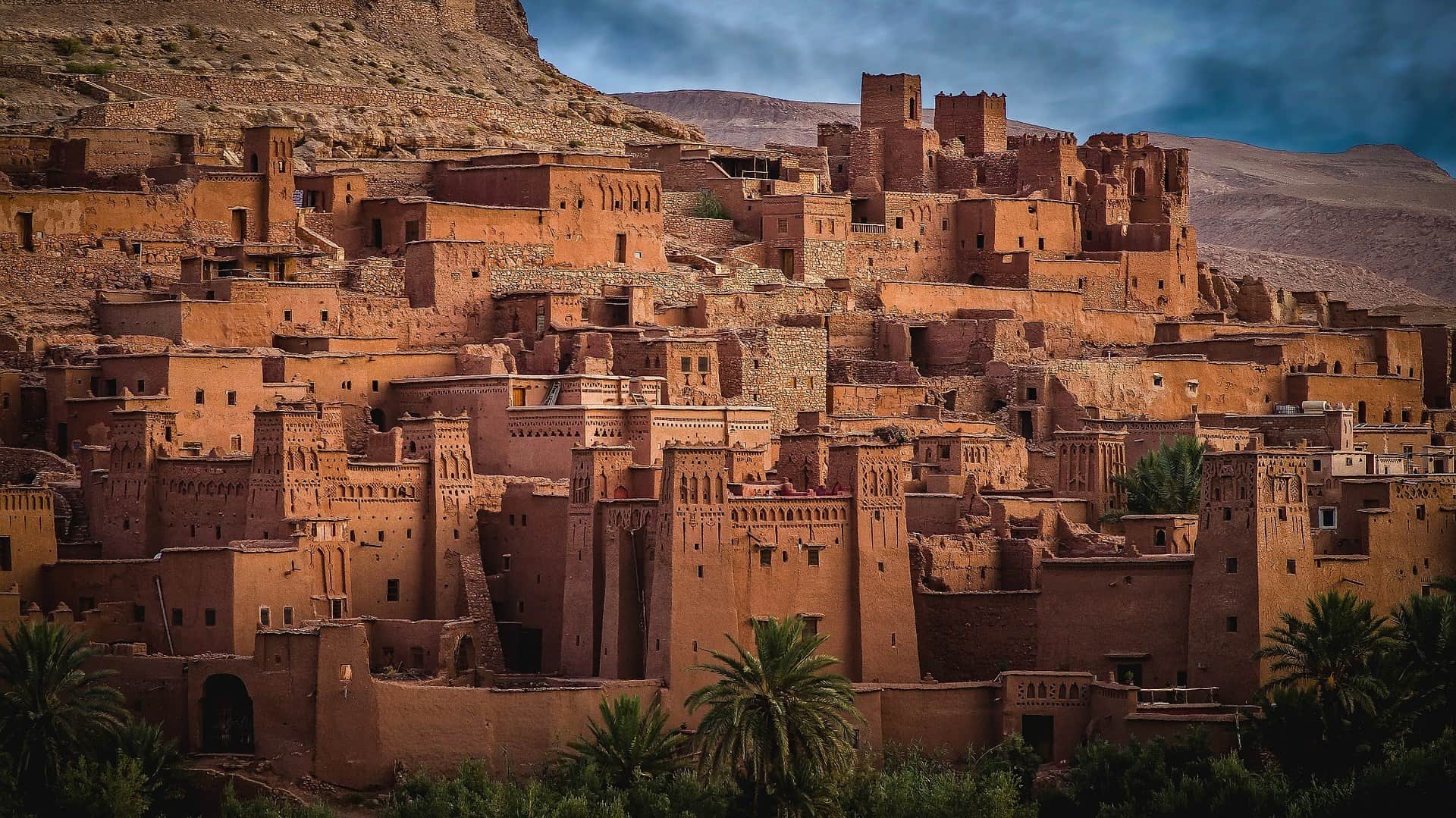 Kasbah de Ait Ben Haddou al atardecer, ksar de barro Patrimonio UNESCO con palmeras en primer plano, Marruecos