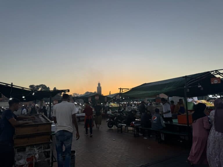 Atardecer en la plaza Jemaa el-Fna de Marrakech con puestos de comida y minarete de la Koutoubia al fondo