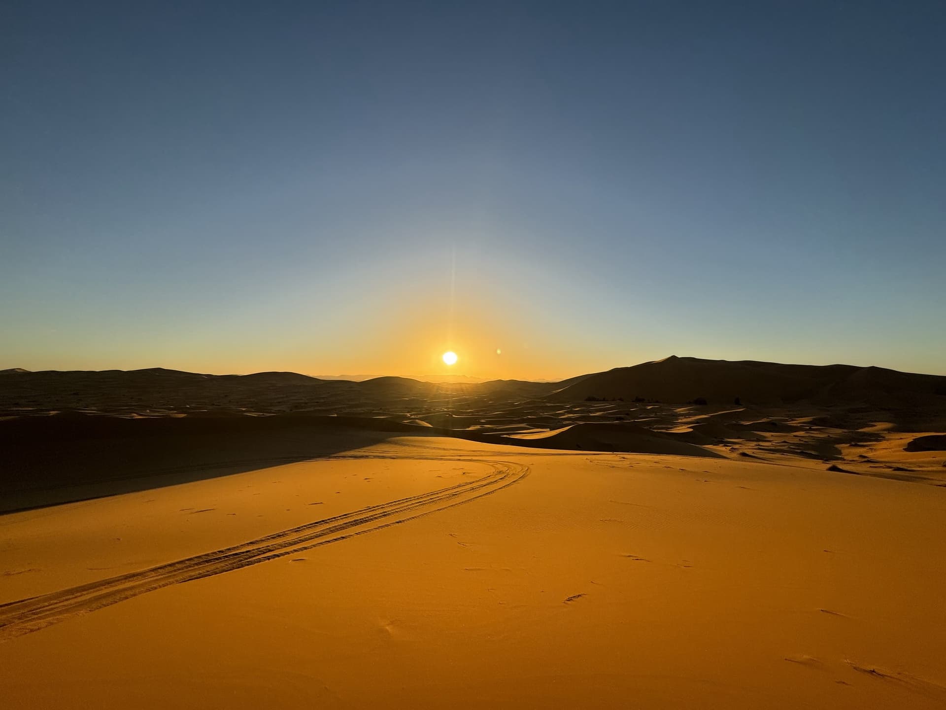 Amanecer dorado sobre las dunas del desierto de Merzouga con huellas de 4x4 en la arena del Erg Chebbi