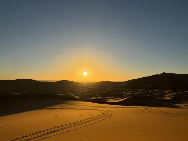 Amanecer dorado sobre las dunas del Erg Chebbi en Merzouga, con huellas de vehículo en la arena del Sahara