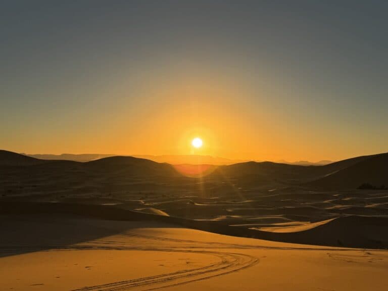 Atardecer dorado sobre las dunas del desierto de Merzouga, Erg Chebbi, con huellas de 4x4 en la arena