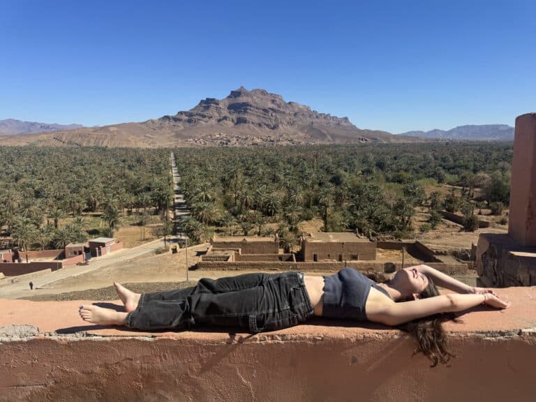 Viajera tumbada en terraza con vistas al oasis de palmeras y montañas del sur de Marruecos