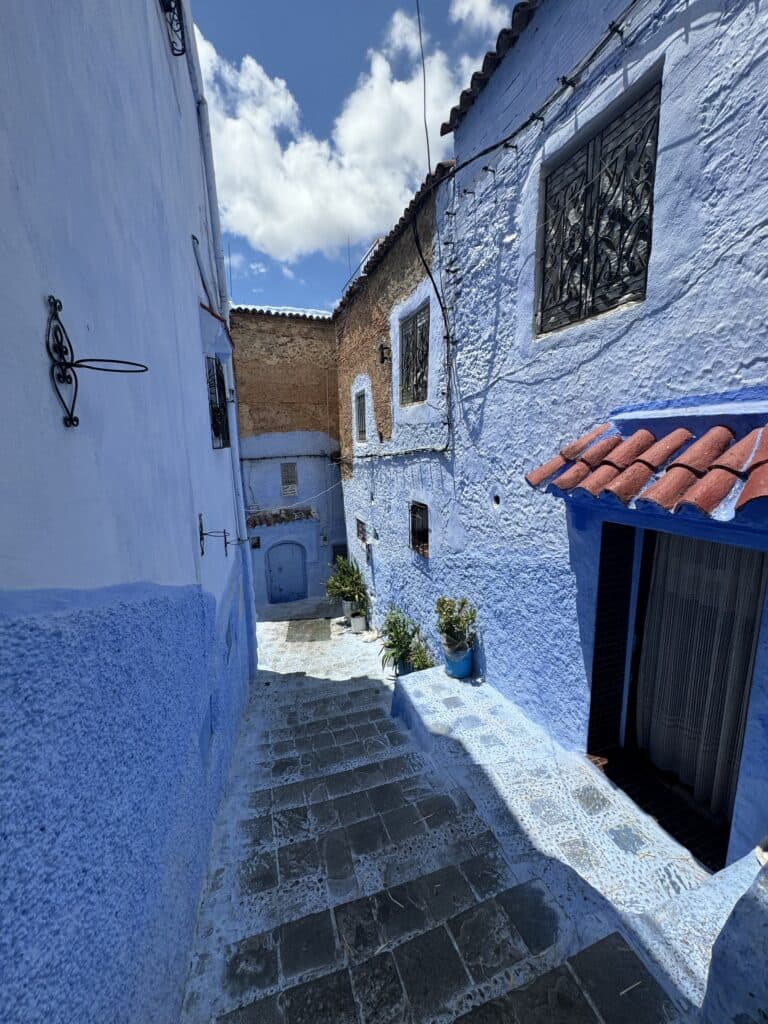 Callejón azul empedrado con escaleras en la medina de Chefchaouen, Marruecos, con macetas y cielo azul