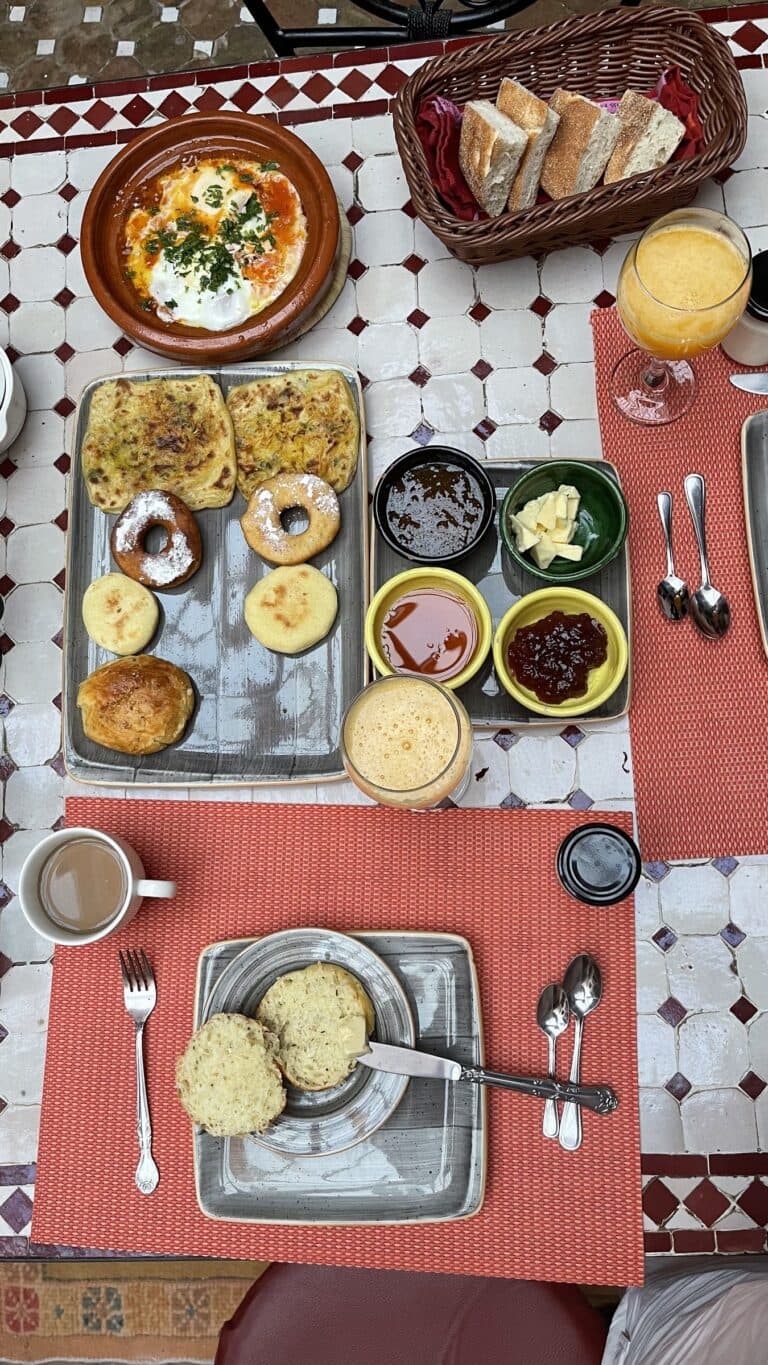 Desayuno marroquí tradicional en riad con msemen, beghrir, harcha, huevos en tajine, miel y zumo de naranja