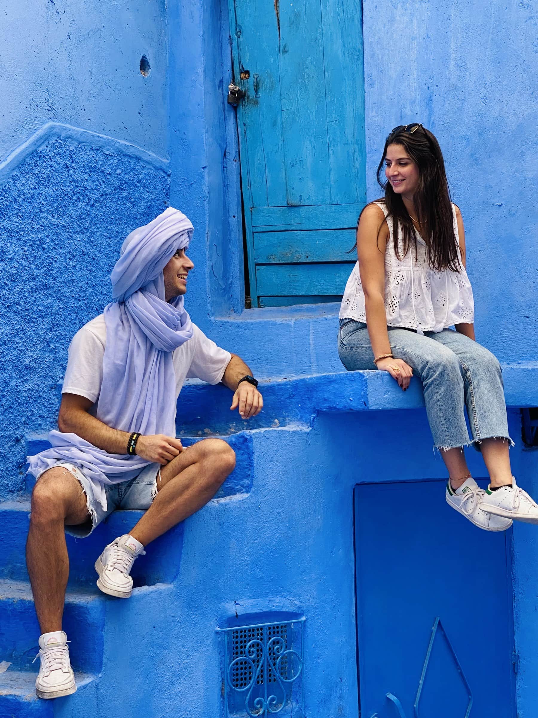 Pareja de viajeros sonriendo en las escaleras azules de la medina de Chefchaouen, Marruecos