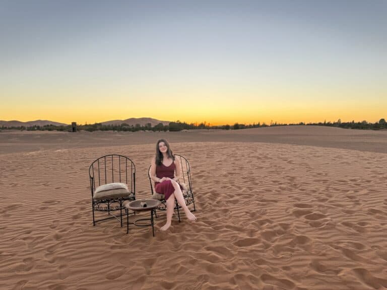 Viajera sentada en sillas de forja en el desierto de Merzouga al atardecer con cielo dorado