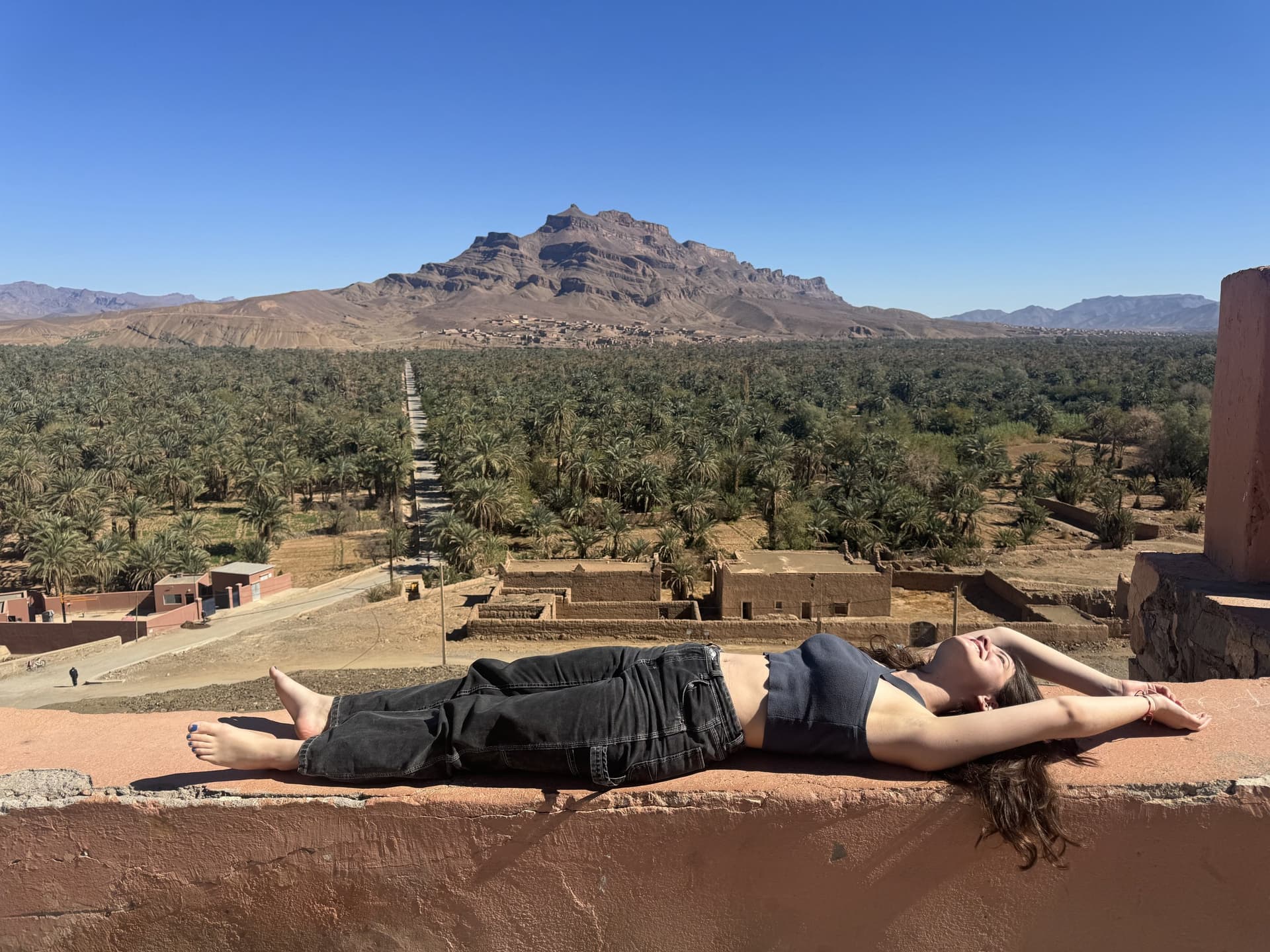 Viajera tumbada en terraza con vistas al oasis de palmeras y montañas del sur de Marruecos