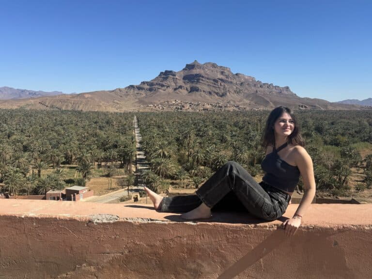 Viajera sentada en terraza con vistas al palmeral del Valle del Draa y montañas rocosas en Marruecos