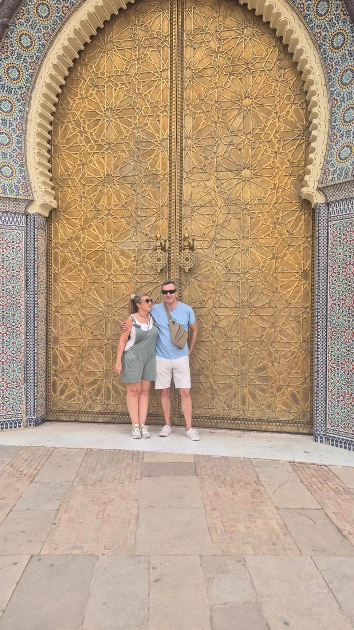 Pareja de viajeros frente a las puertas doradas del Palacio Real de Fez con mosaicos de zellige