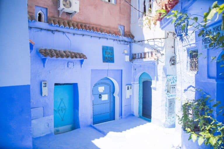 Callejón azul de Chefchaouen con puertas moriscas y cartel del Riad Yazio en la medina de Marruecos