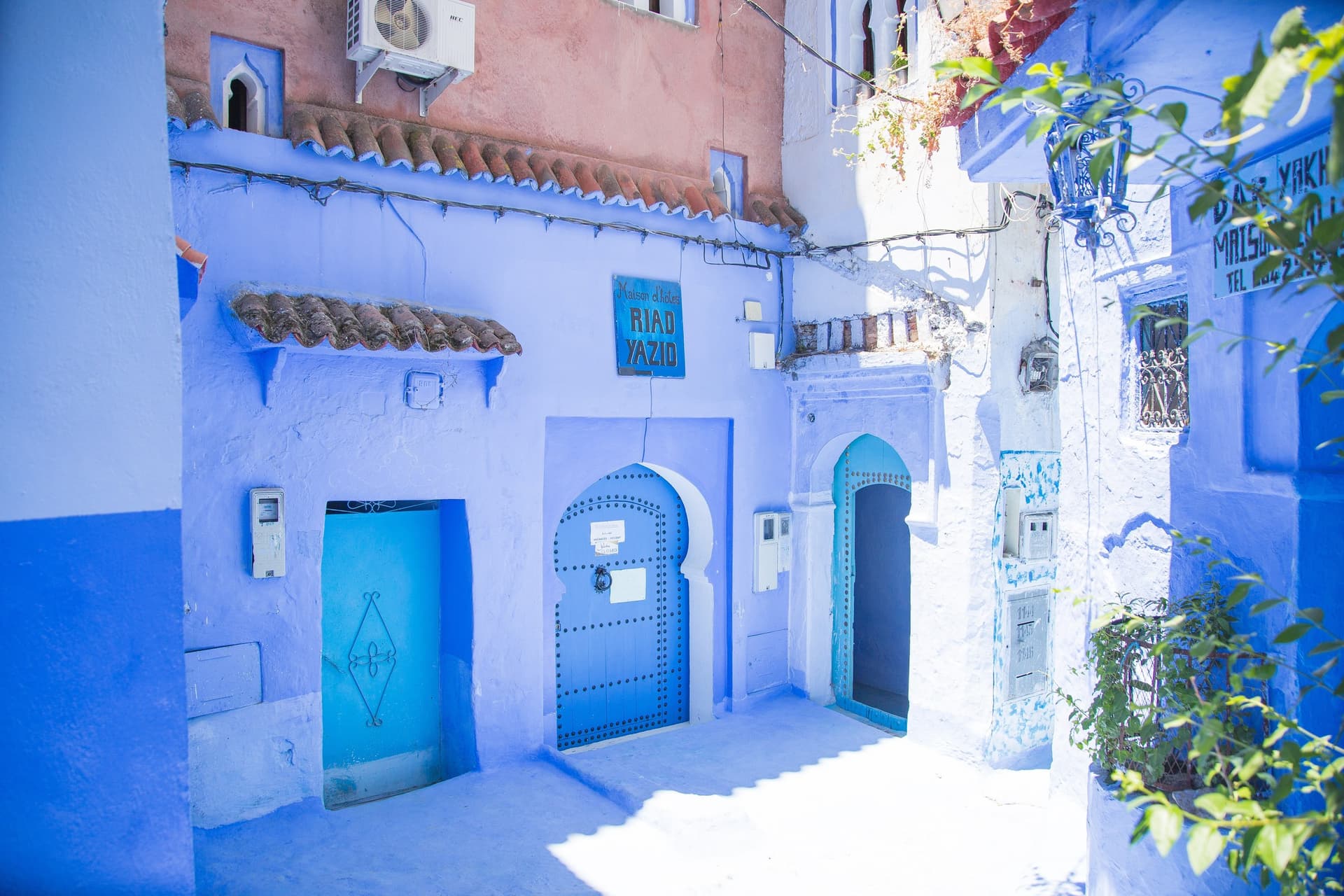 Callejón azul de Chefchaouen con puertas moriscas y cartel del Riad Yazio en la medina de Marruecos